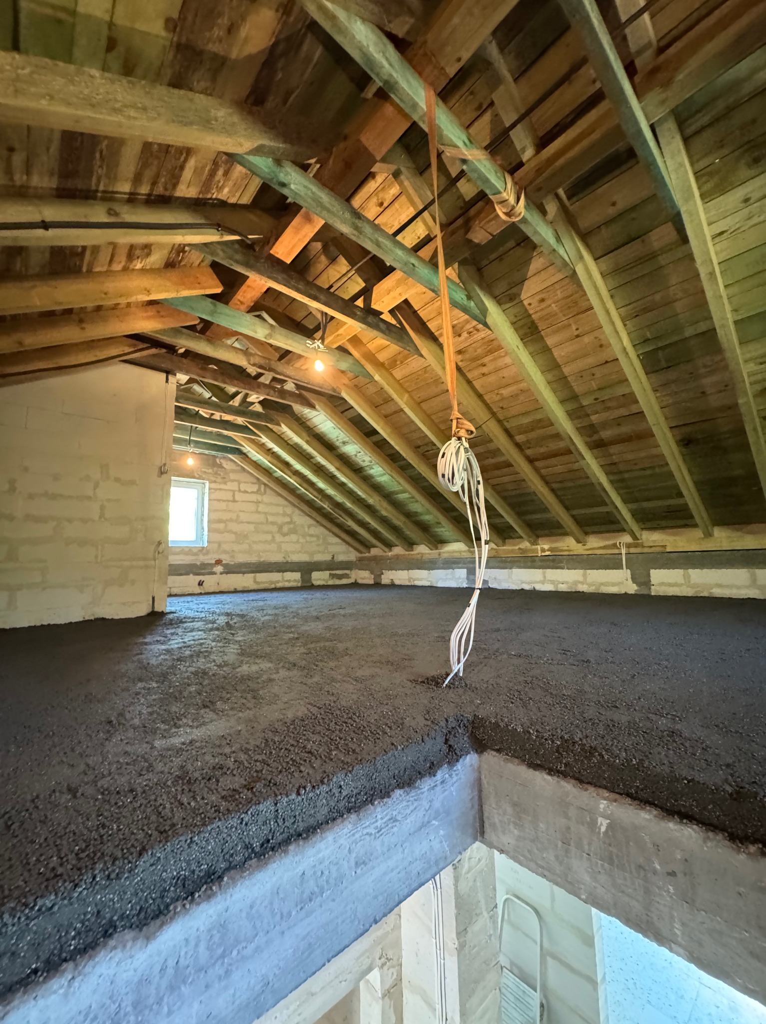 Wylana posadzka jastrychowa na poddaszu w Piastowie. Widoczne drewniane belki stropowe i ściany z bloczków. Szara, gładka powierzchnia jastrychu.