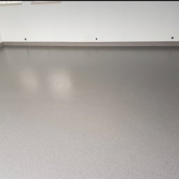 SOBOL - Gładka, szara posadzka w pustym pomieszczeniu z białymi ścianami i szarymi listwami przypodłogowymi, widoczne punkty mocowania listew.