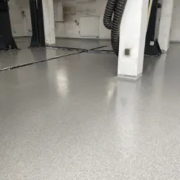 Błyszcząca, jasnoszara posadzka w hali warsztatowej z podnośnikami samochodowymi. Nowa, gładka powierzchnia, z widocznymi szczelinami dylatacyjnymi.