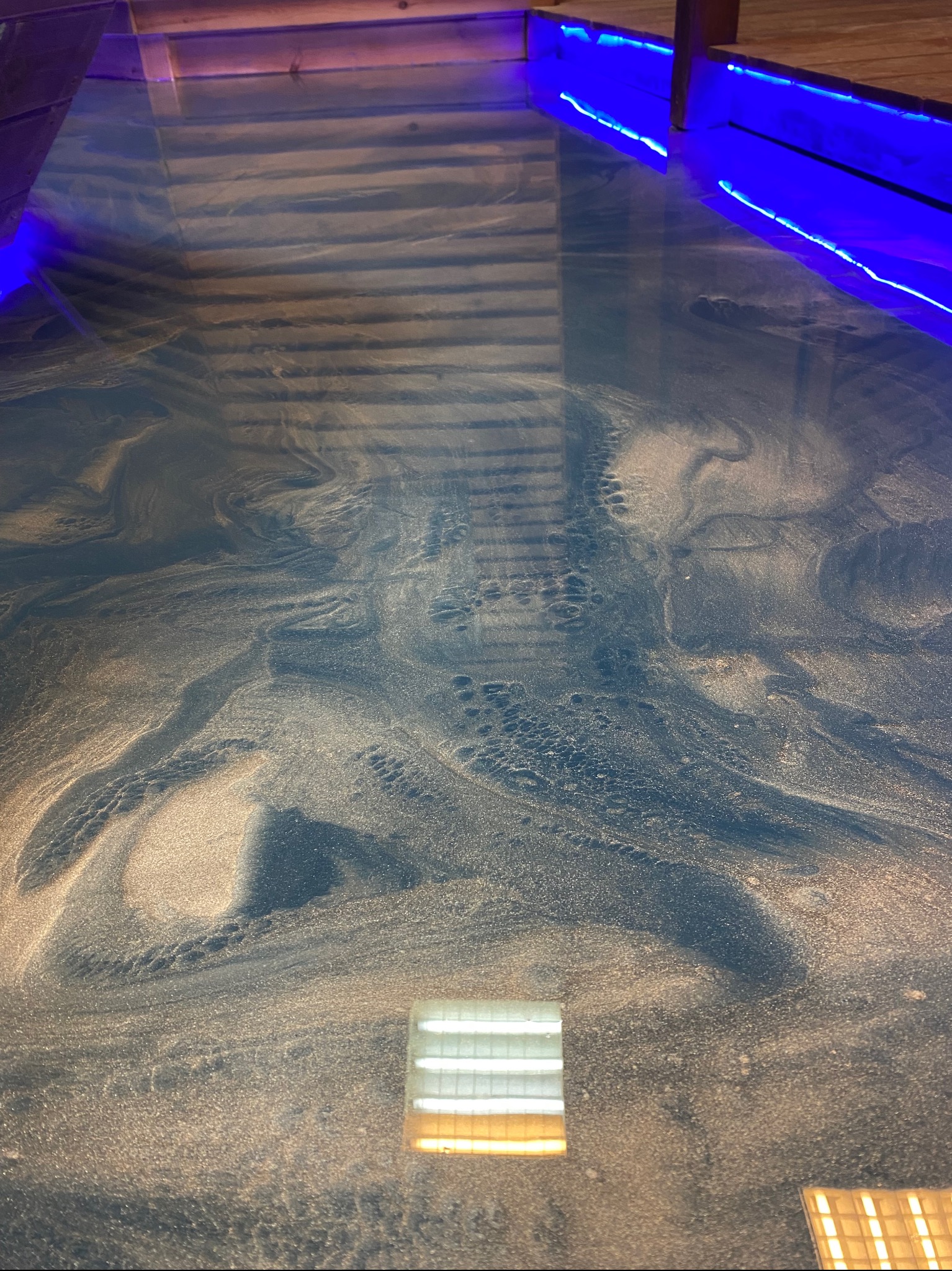 Błyszcząca, ciemnoniebieska podłoga z efektem marmuru i złotymi żyłkami, oświetlona niebieskim światłem LED wzdłuż krawędzi i lampą podsufitową.