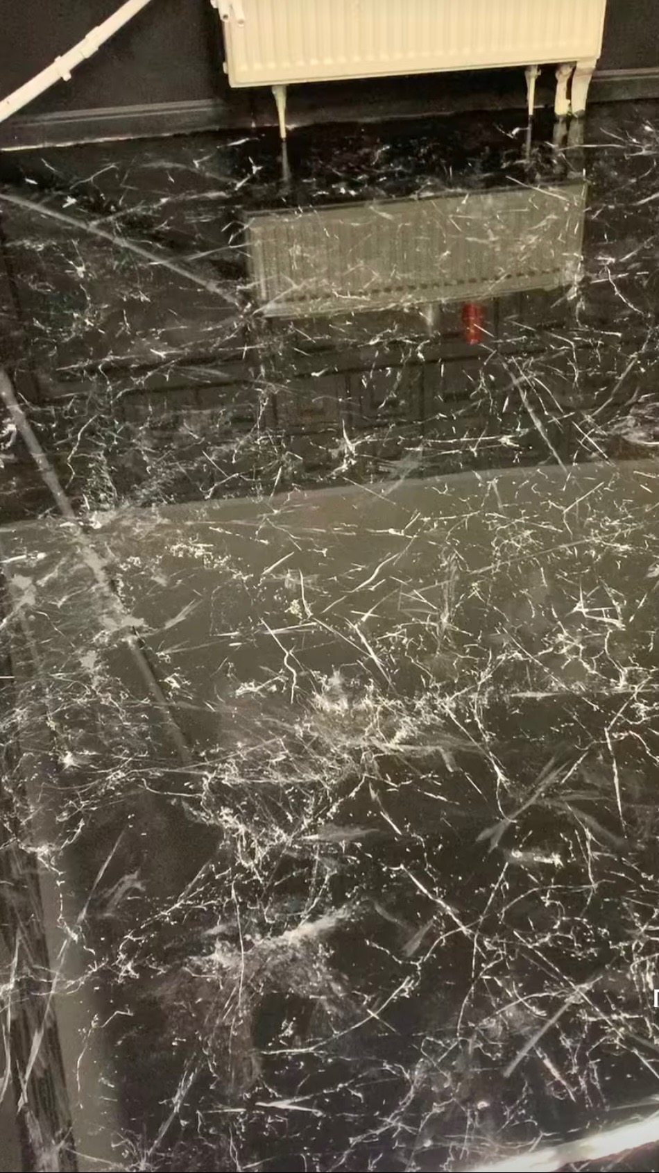 Czarna posadzka z białymi żyłkami imitującymi marmur, zabezpieczona folią ochronną, widoczny grzejnik na ścianie.