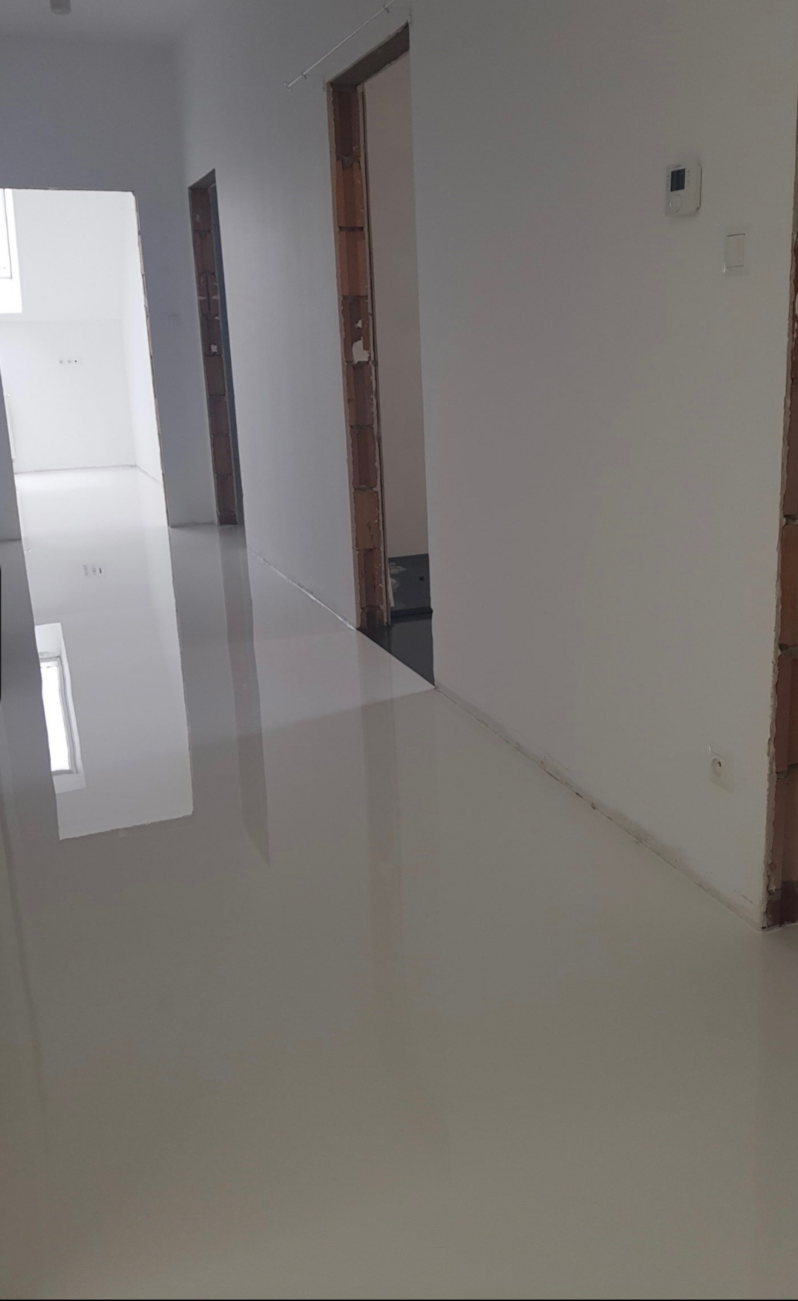 Błyszcząca, jasna posadzka w korytarzu w trakcie remontu w Warszawie, widoczne surowe ościeżnice drzwiowe i białe ściany.