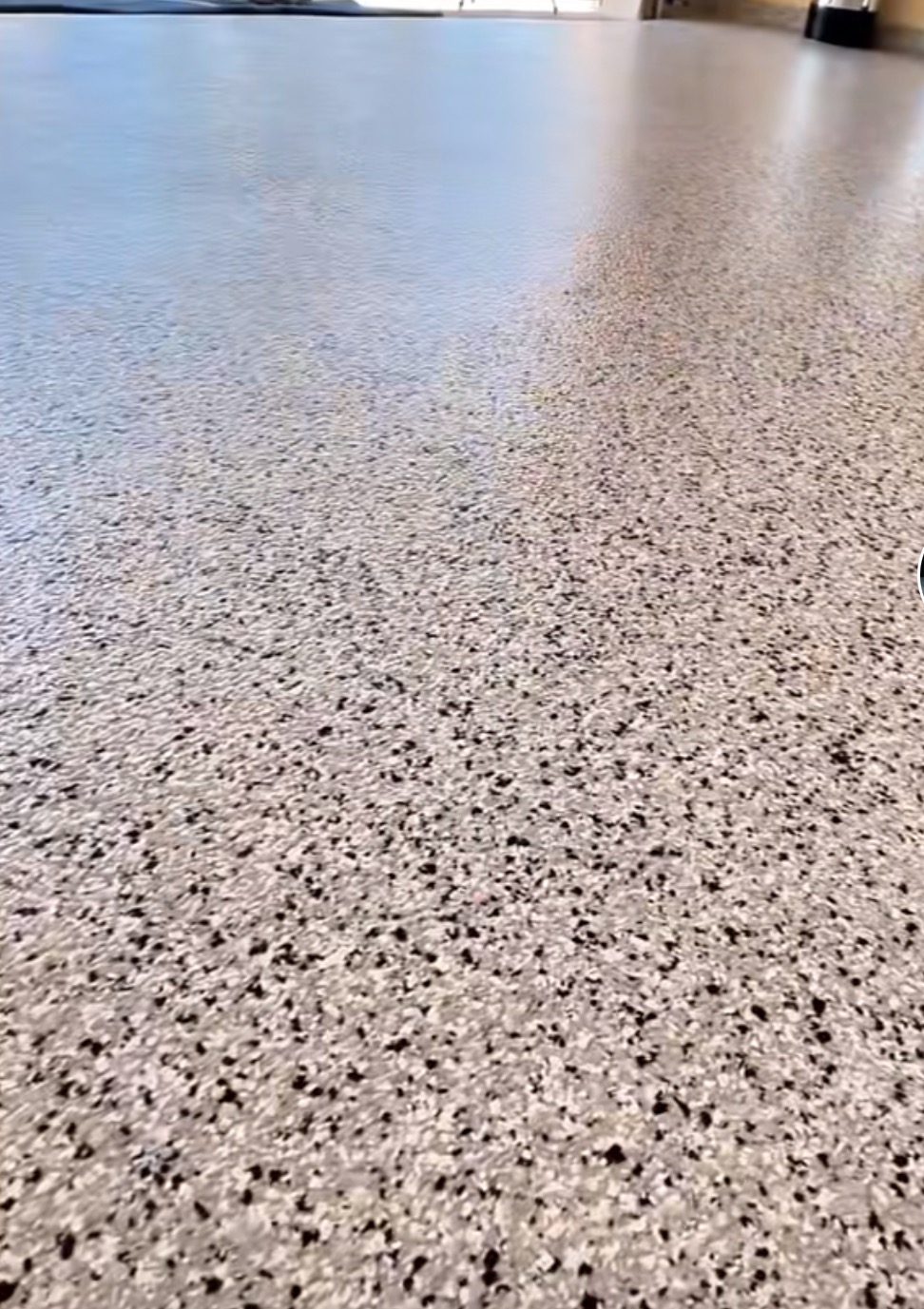 Błyszcząca, gładka posadzka z żywicy epoksydowej w garażu, wykończona drobnymi, czarnymi i szarymi płatkami dekoracyjnymi, tworzącymi wzór lastryko.