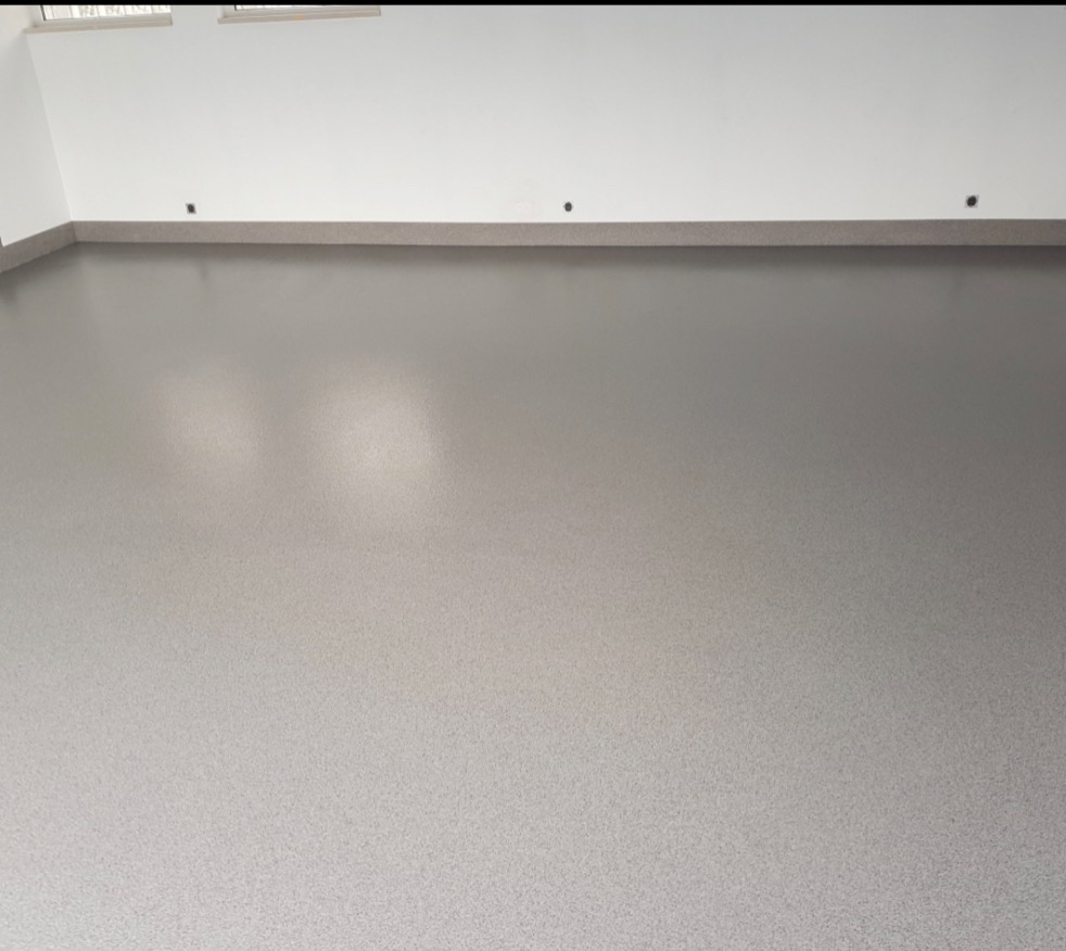 Gładka, szara posadzka w pustym pomieszczeniu z białymi ścianami i szarymi listwami przypodłogowymi, widoczne punkty mocowania listew.