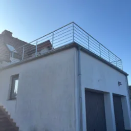 Nowoczesna, minimalistyczna balustrada ze stali nierdzewnej na dachu budynku z garażem, widok z dołu, błękitne niebo w tle.