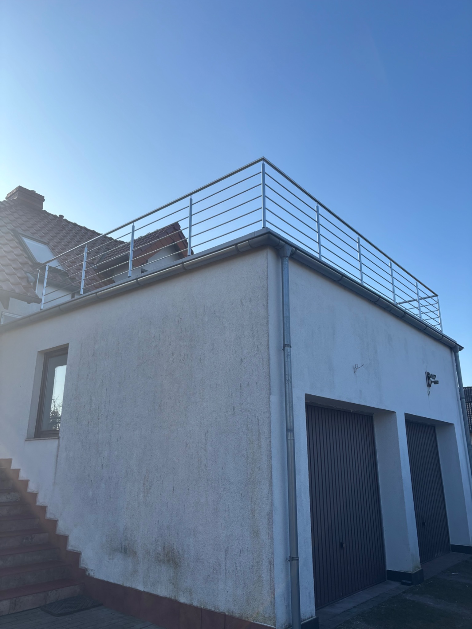 Nowoczesna, minimalistyczna balustrada ze stali nierdzewnej na dachu budynku z garażem, widok z dołu, błękitne niebo w tle.