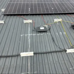 Instalacja paneli fotowoltaicznych na blaszanym dachu w Rokitnie, widoczne kable, moduły i skrzynki przyłączeniowe, częściowo zamontowane.