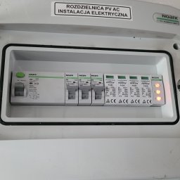 PIEDOX Piotr Pałka - Otwarta skrzynka rozdzielcza PV AC z zainstalowanymi zabezpieczeniami przepięciowymi i wyłącznikami nadprądowymi marki Noark i Fatech, widoczne diody sygnalizacyjne stanu.