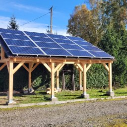 PIEDOX Piotr Pałka - Drewniana wiata z panelami słonecznymi na dachu, widoczna w słoneczny dzień na tle zieleni.