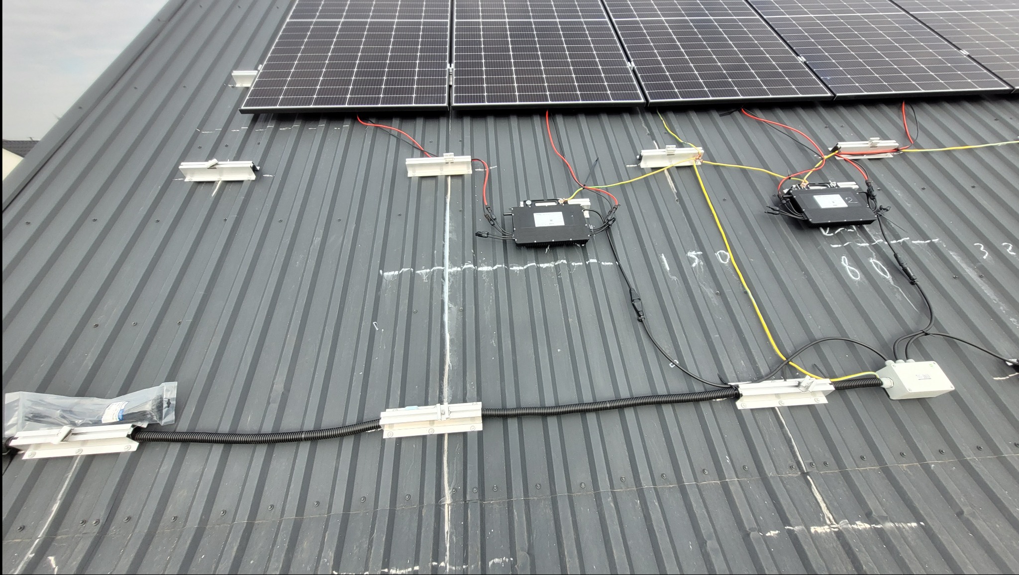 Instalacja paneli fotowoltaicznych na blaszanym dachu w Rokitnie, widoczne kable, moduły i skrzynki przyłączeniowe, częściowo zamontowane.