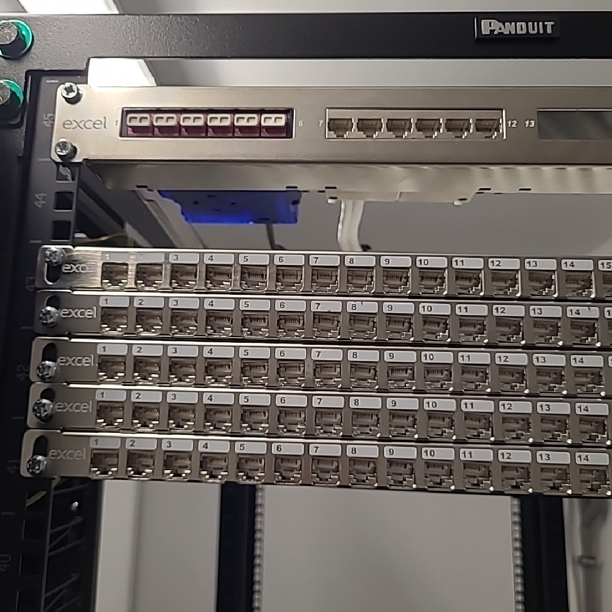 Panel krosowniczy Excel zamontowany w szafie serwerowej, widoczne porty RJ45 z numeracją, górny panel z częściowo podłączonymi kablami.