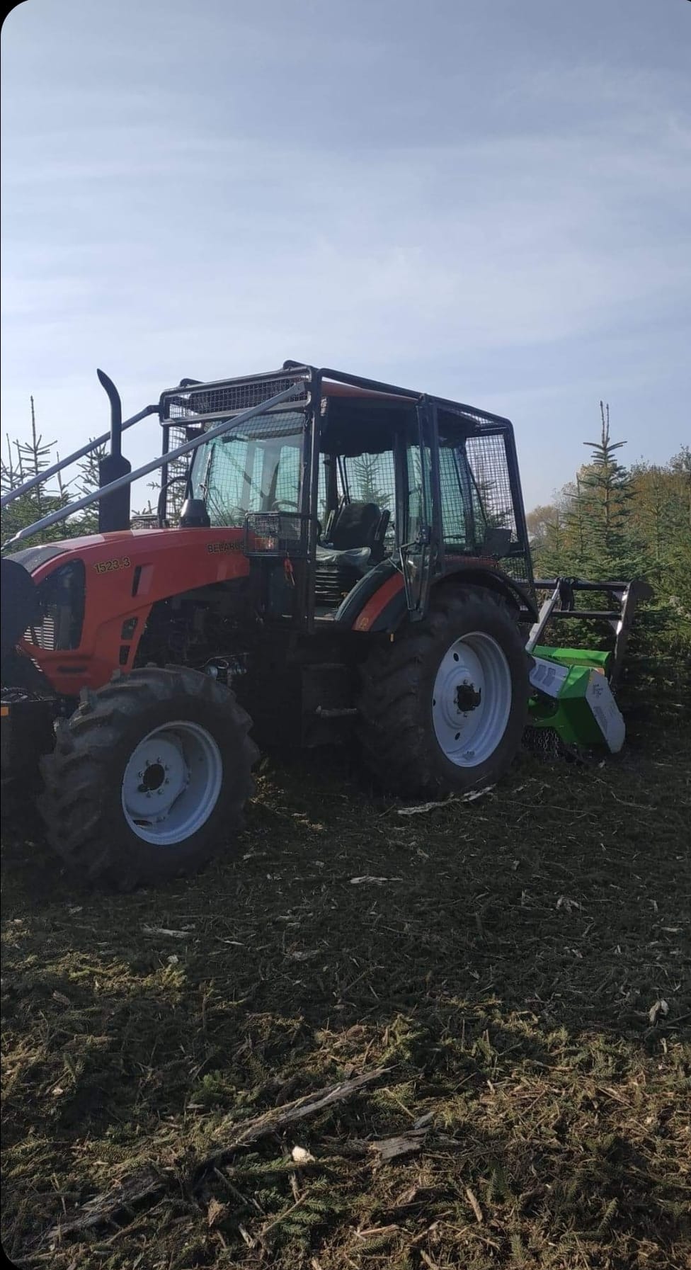 Czerwony traktor z osłoną kabiny i frezem do pni na polu po wycince drzew, widoczne ślady po cięciu i pozostałości gałęzi.