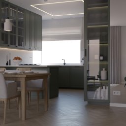 NATALIA MACKO Studio Wymiar Architektura Wnętrz - Nowoczesna kuchnia w odcieniach zieleni z drewnianym stołem jadalnym, białymi krzesłami i dekoracyjną ścianą z roślin.