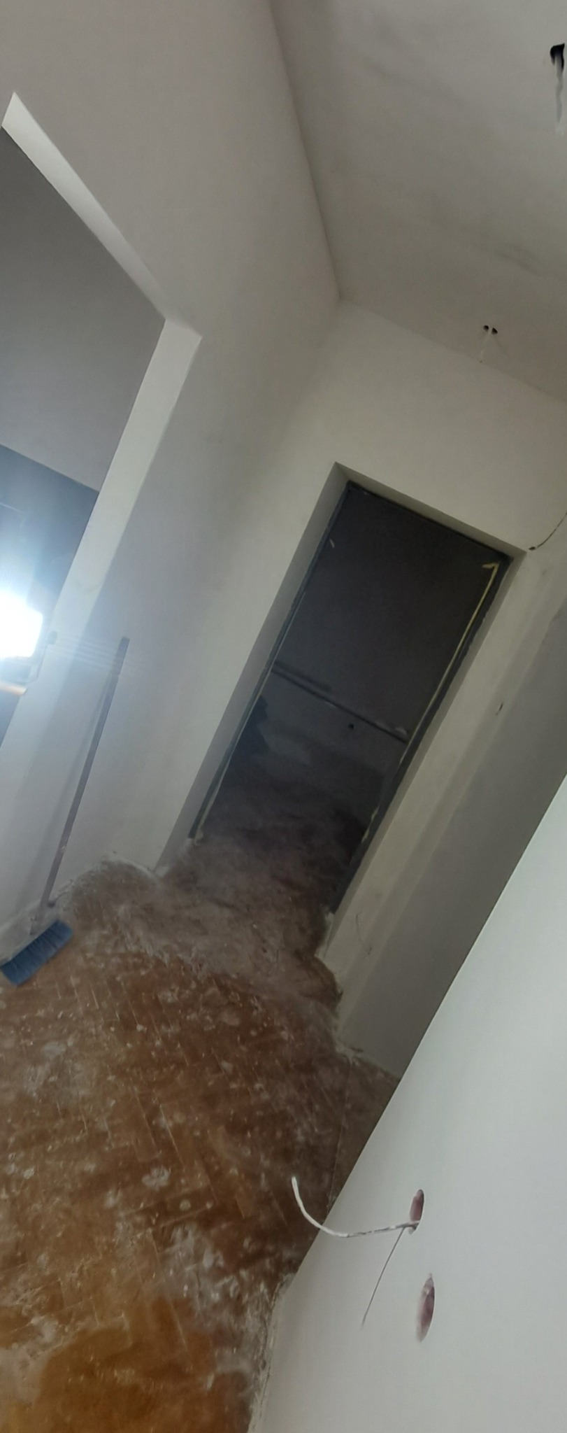 Wnętrze w trakcie prac wykończeniowych: ściany po nałożeniu gładzi, widoczne otwory na gniazdka elektryczne z wystającymi przewodami, podłoga zabezpieczona folią i resztki materiałów budowlanych...