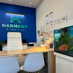 HARMONY FINANSE SPÓŁKA Z OGRANICZONĄ ODPOWIEDZIALNOŚCIĄ - Biuro Harmony Finanse z akwarium, biurkiem, krzesłami i logo na niebieskiej ścianie, certyfikaty w ramkach na ścianie
