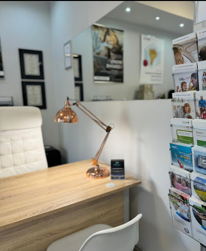 Jasne biuro z drewnianym biurkiem, miedzianą lampką, białym krzesłem i ulotkami w tle, prawdopodobnie punkt obsługi klienta.