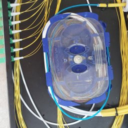 NetVolt Łukasz Martin - Rozdzielnica światłowodowa z żółtymi i białymi kablami światłowodowymi, z widocznym splajsem światłowodowym AFL Hyperscale w niebieskiej obudowie.