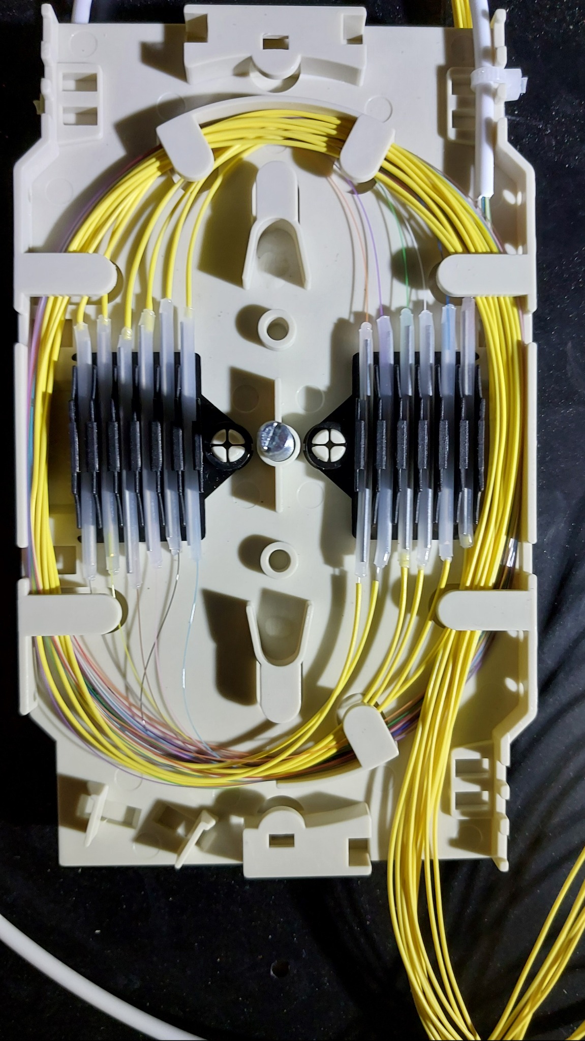 Rozdzielnica światłowodowa z żółtymi kablami i złączkami, widok z góry na wnętrze skrzynki.