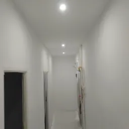 Korytarz w Szczecinie po remoncie, świeżo pomalowane na biało ściany i sufit z trzema punktowymi lampami LED, widoczne drzwi z futrynami przygotowane do montażu.