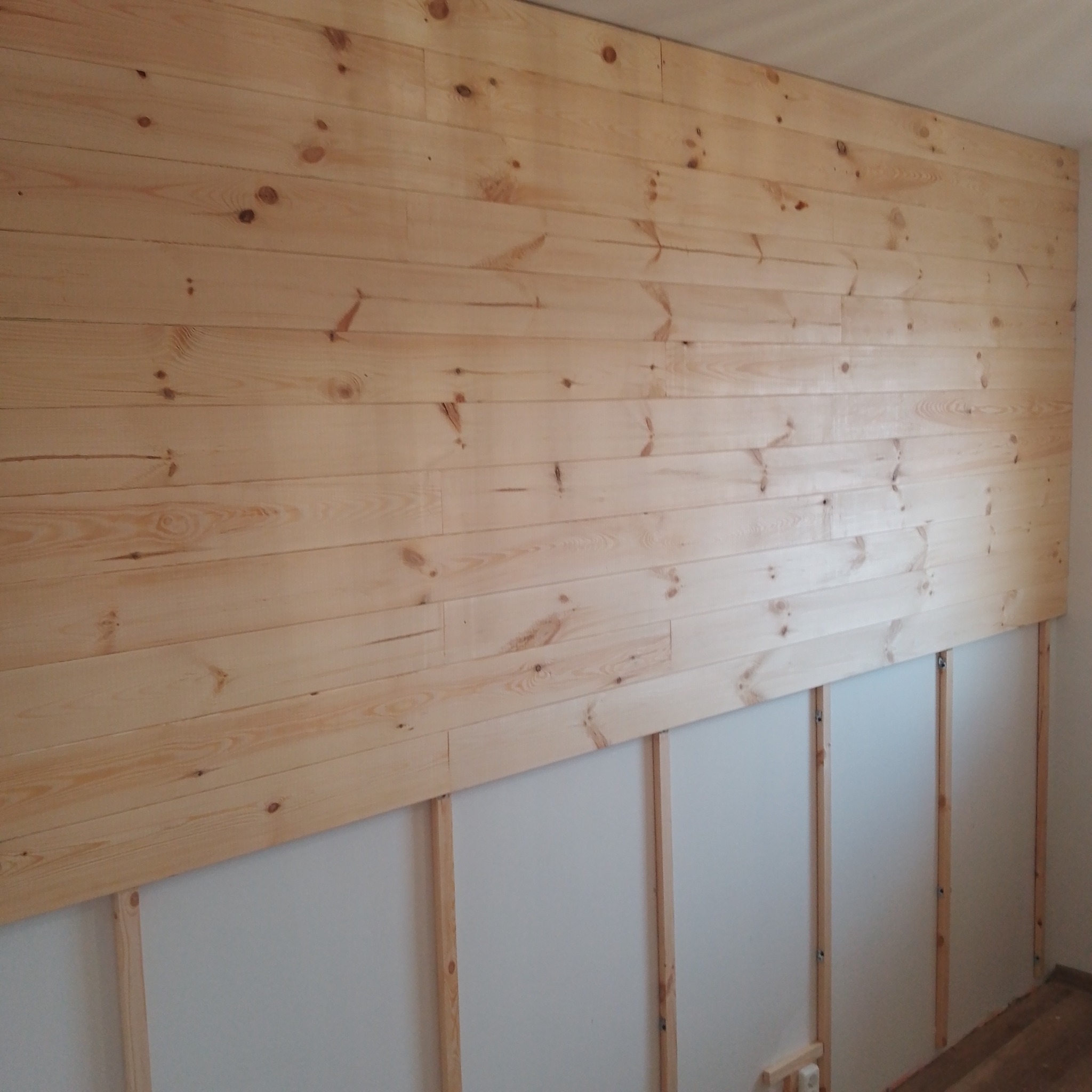 Ściana w trakcie wykańczania drewnianą boazerią, widoczne listwy montażowe i fragment surowej ściany.