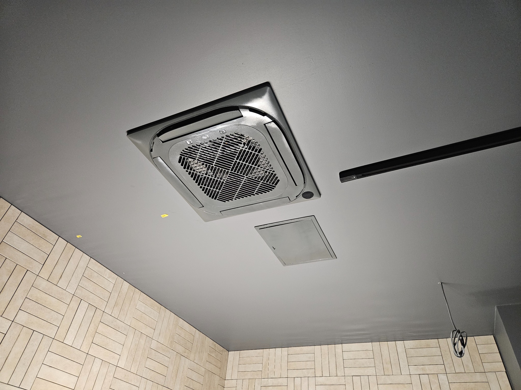 Sufitowa kaseta klimatyzacyjna w biurze, widok z dołu, obok widoczny panel dostępowy i szyna oświetleniowa.