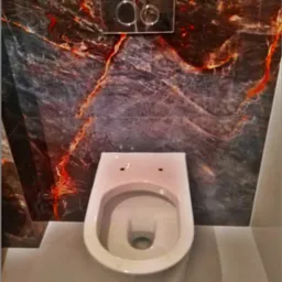 Zamontowana podwieszana toaleta z chromowanym przyciskiem spłukującym na ścianie wyłożonej płytkami imitującymi ciemny marmur z czerwonymi żyłkami, widok z góry, Kraków.