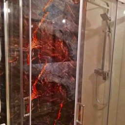 MARKBUD MAREK NEUDECK - Kabina prysznicowa z przesuwnymi drzwiami, wyłożona płytkami imitującymi ciemny marmur z czerwonymi żyłami, widoczna bateria i słuchawka prysznicowa.