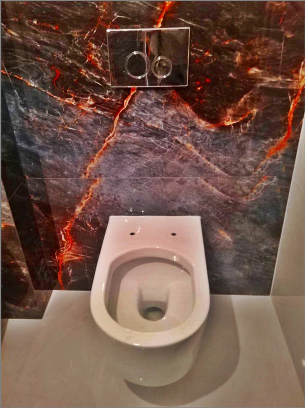 Zamontowana podwieszana toaleta z chromowanym przyciskiem spłukującym na ścianie wyłożonej płytkami imitującymi ciemny marmur z czerwonymi żyłkami, widok z góry, Kraków.