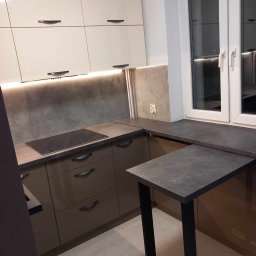 KONRAD-MEBLE - Nowoczesna kuchnia z beżowymi szafkami górnymi, brązowymi dolnymi, szarym blatem i wysuwanym, czarnym stołem, oświetlona listwą LED pod szafkami.