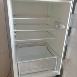 Wnętrze pustej, otwartej lodówki z półkami z przezroczystego szkła i plastikową szufladą na warzywa.