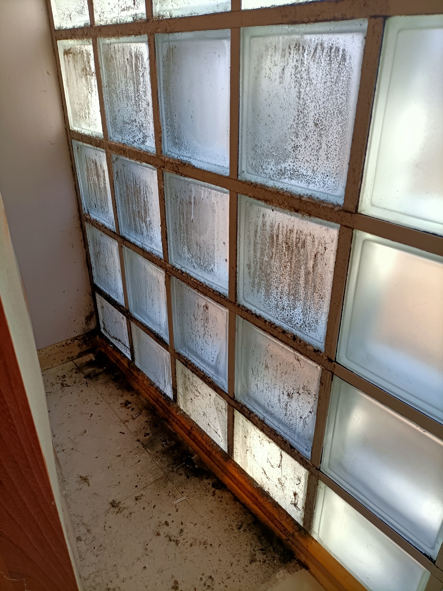 Zabrudzone luksfery z widocznymi zaciekami i osadami, osadzone w ramie, zanieczyszczona podłoga w tle.