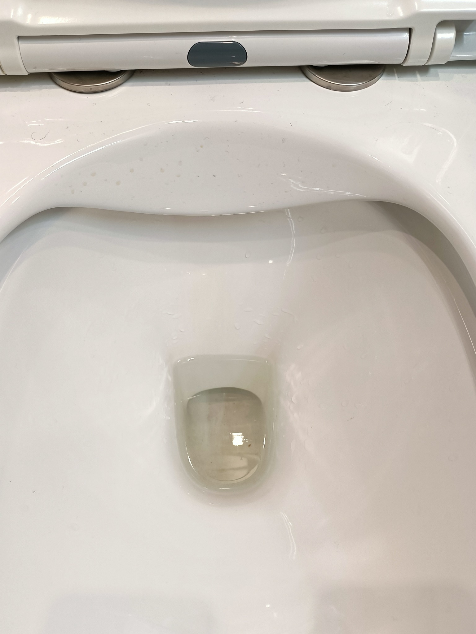 Biała, ceramiczna toaleta z widocznymi śladami po czyszczeniu i kroplami wody.