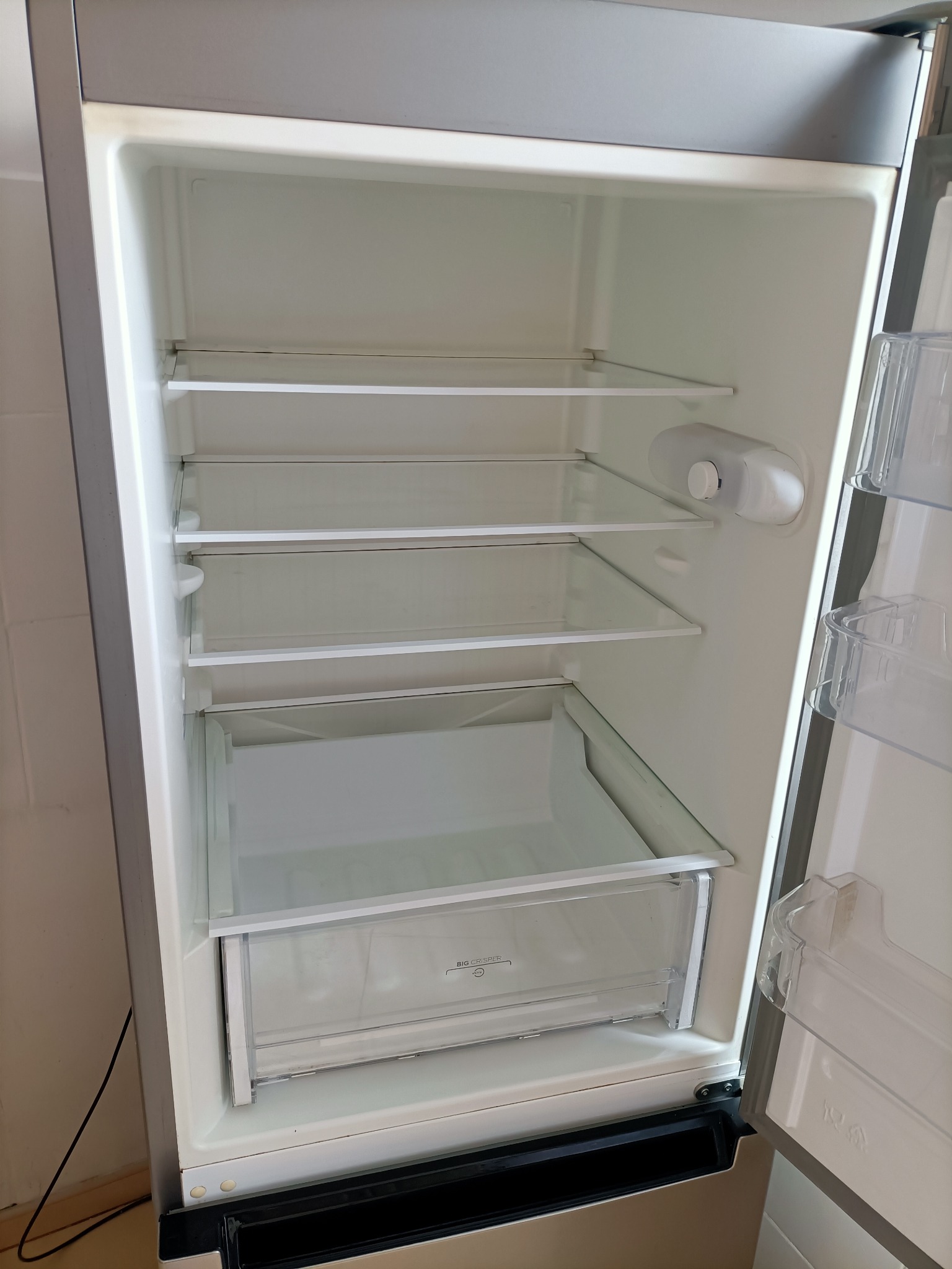 Wnętrze pustej, otwartej lodówki z półkami z przezroczystego szkła i plastikową szufladą na warzywa.