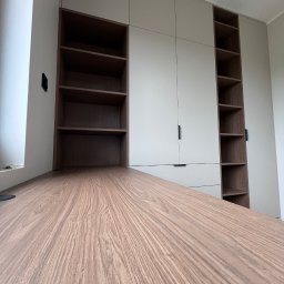 MD STUDIO MEBLE NA WYMIAR Maja Dziedzic - Jasnoszara szafa wnękowa z ciemnymi półkami i biurkiem z drewnianym blatem. Minimalistyczny design, nowoczesne wykończenie, widok z dołu.