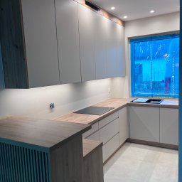 MD STUDIO MEBLE NA WYMIAR Maja Dziedzic - Nowoczesna kuchnia z jasnymi szafkami i drewnianym blatem. Okno zabezpieczone folią. Widoczne oświetlenie punktowe i płyta indukcyjna. Minimalistyczny design.