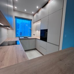 MD STUDIO MEBLE NA WYMIAR Maja Dziedzic - Nowoczesna kuchnia z jasnymi frontami i drewnianym blatem. Okno zabezpieczone folią. Oświetlenie punktowe i podszafkowe. Minimalistyczny design, zabudowa pod sufit.