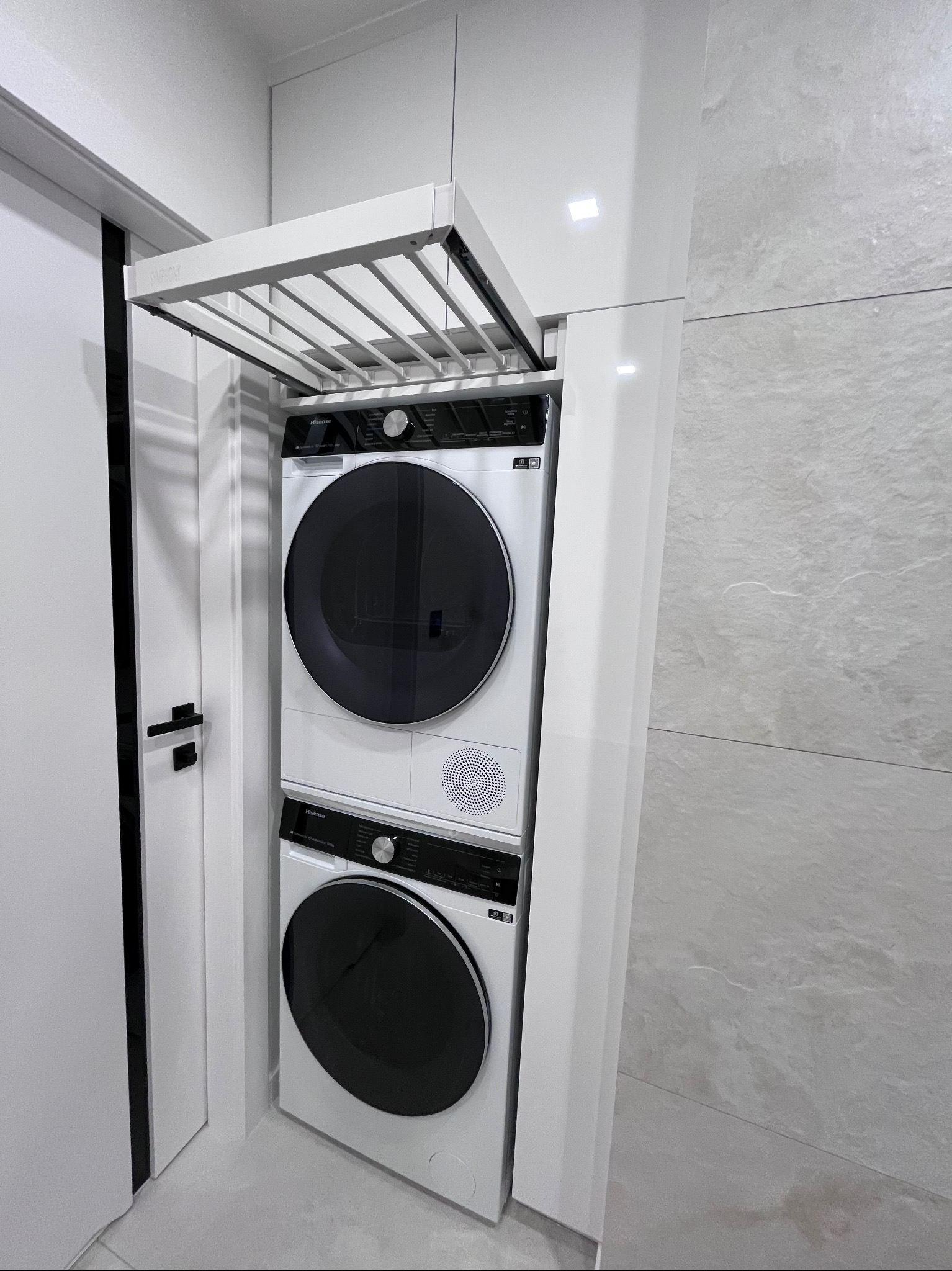 Biała pralka i suszarka w zabudowie meblowej z wysuwaną suszarką podsufitową. Minimalistyczny design, nowoczesne rozwiązanie do małych przestrzeni.