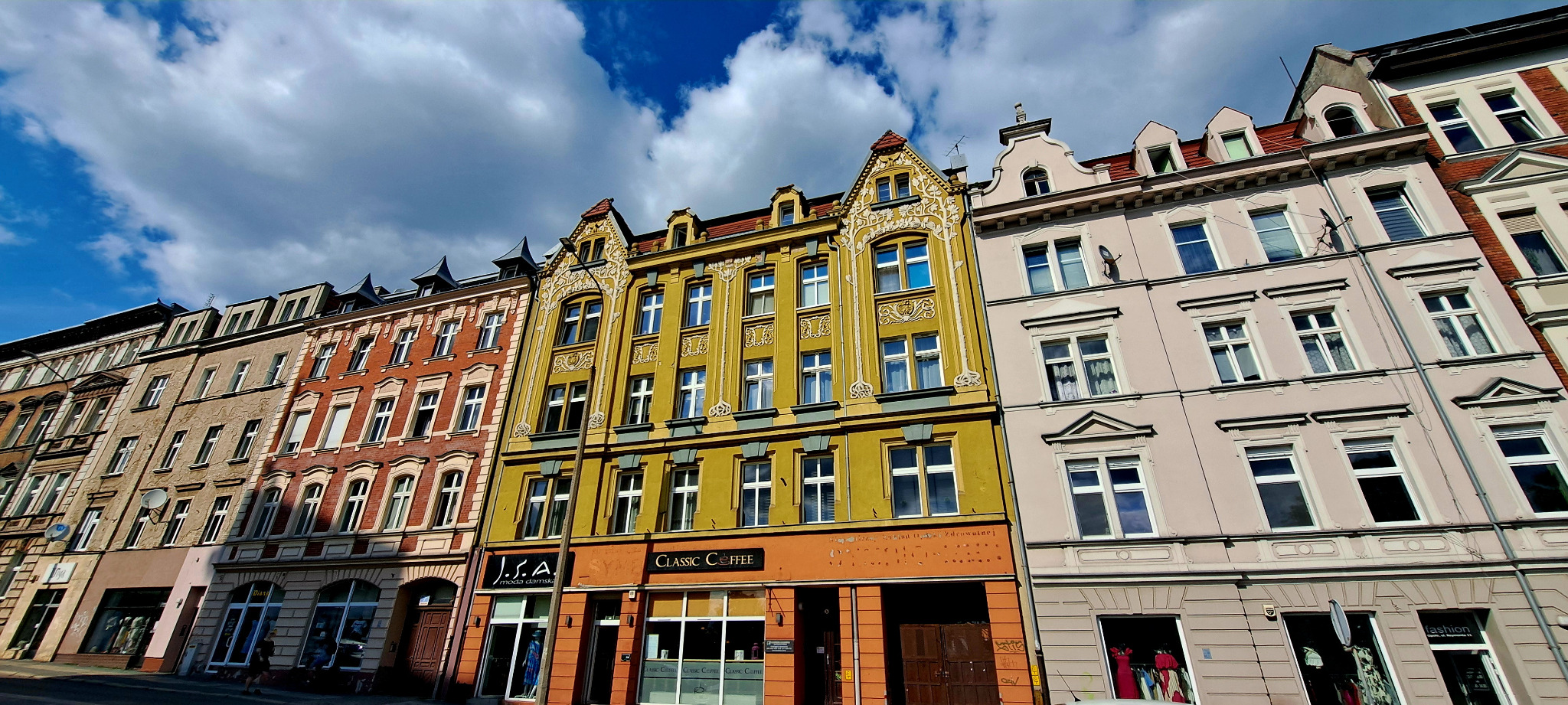 Kolorowe kamienice z odnowionymi fasadami w Opolu, widok z dołu na błękitne niebo z chmurami.
