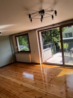 Jasny parkiet w salonie z wyjściem na taras. Widoczne okno z parapetem i grzejnikiem. Nowoczesna lampa sufitowa. Naturalne światło podkreśla połysk drewna.