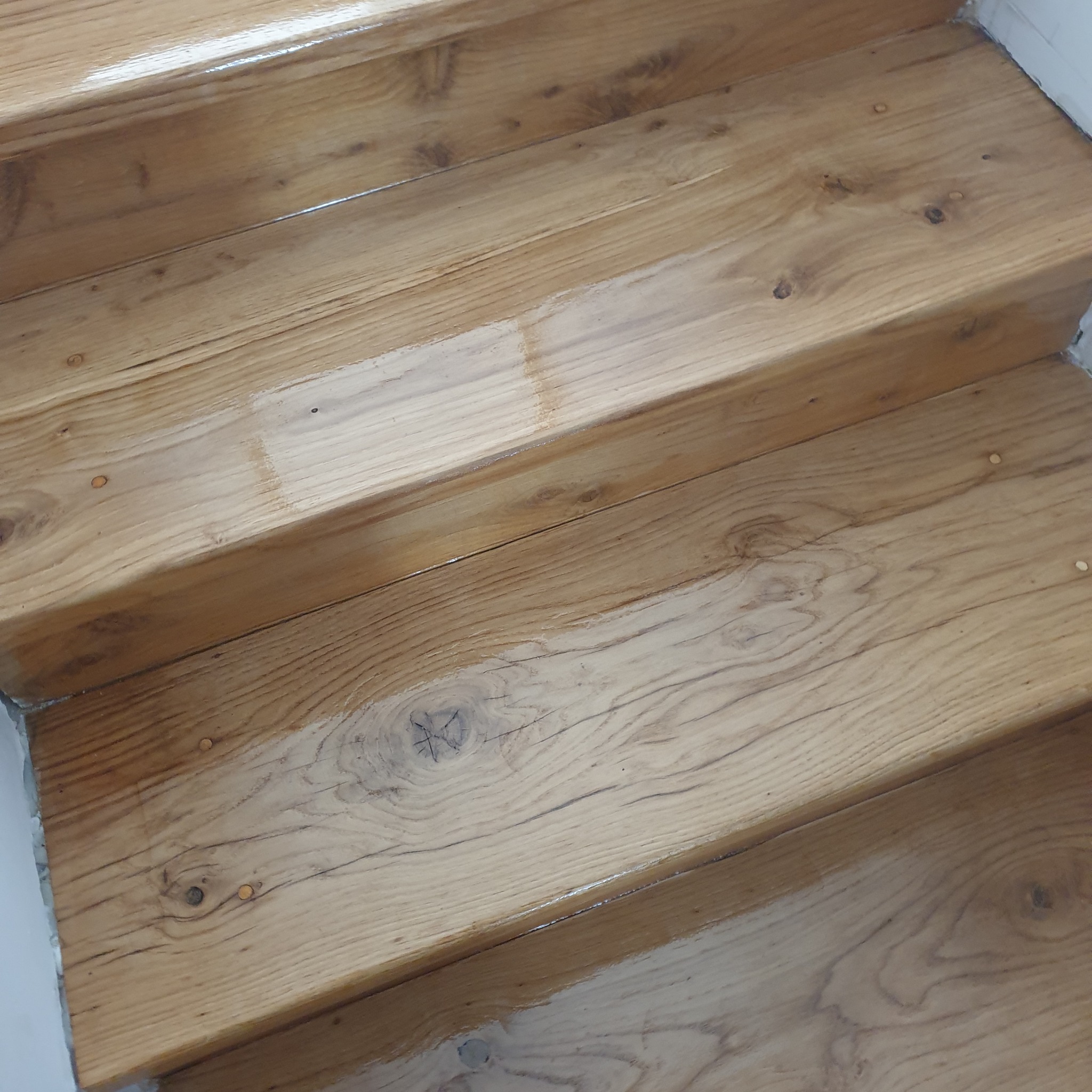 Odnowione drewniane schody z widoczną strukturą drewna i gładką, lakierowaną powierzchnią. Jasne, naturalne odcienie drewna.