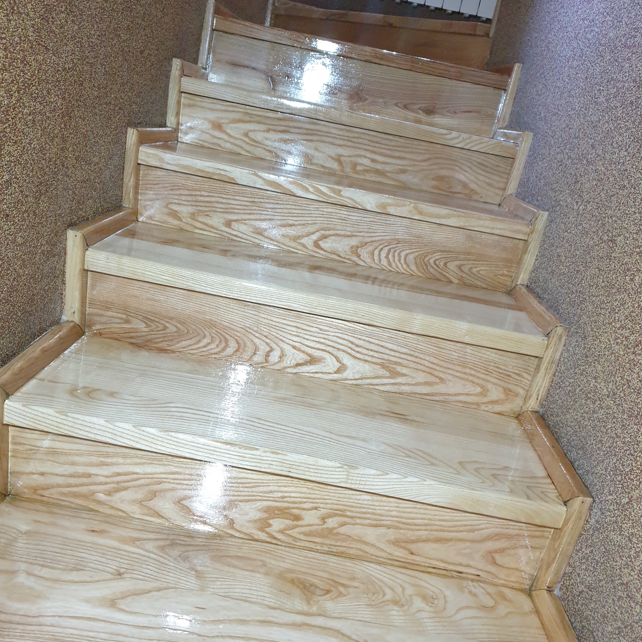 Jasne, drewniane schody po renowacji, widok z góry. Połyskująca powierzchnia, widoczny rysunek drewna. Teksturowana ściana w tle.