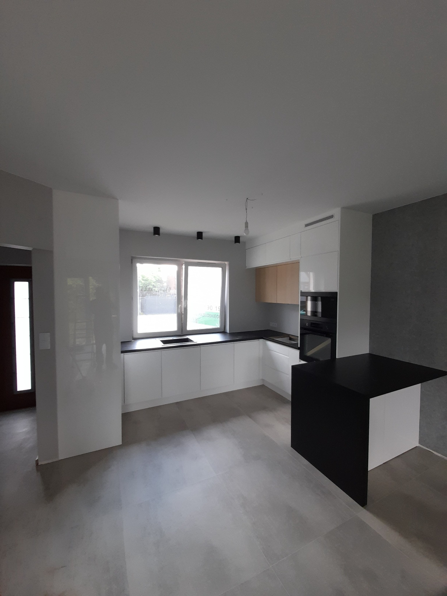 Nowoczesna kuchnia w Zielonce z białymi szafkami, czarnym blatem i wyspą, oświetlona światłem dziennym wpadającym przez okno.