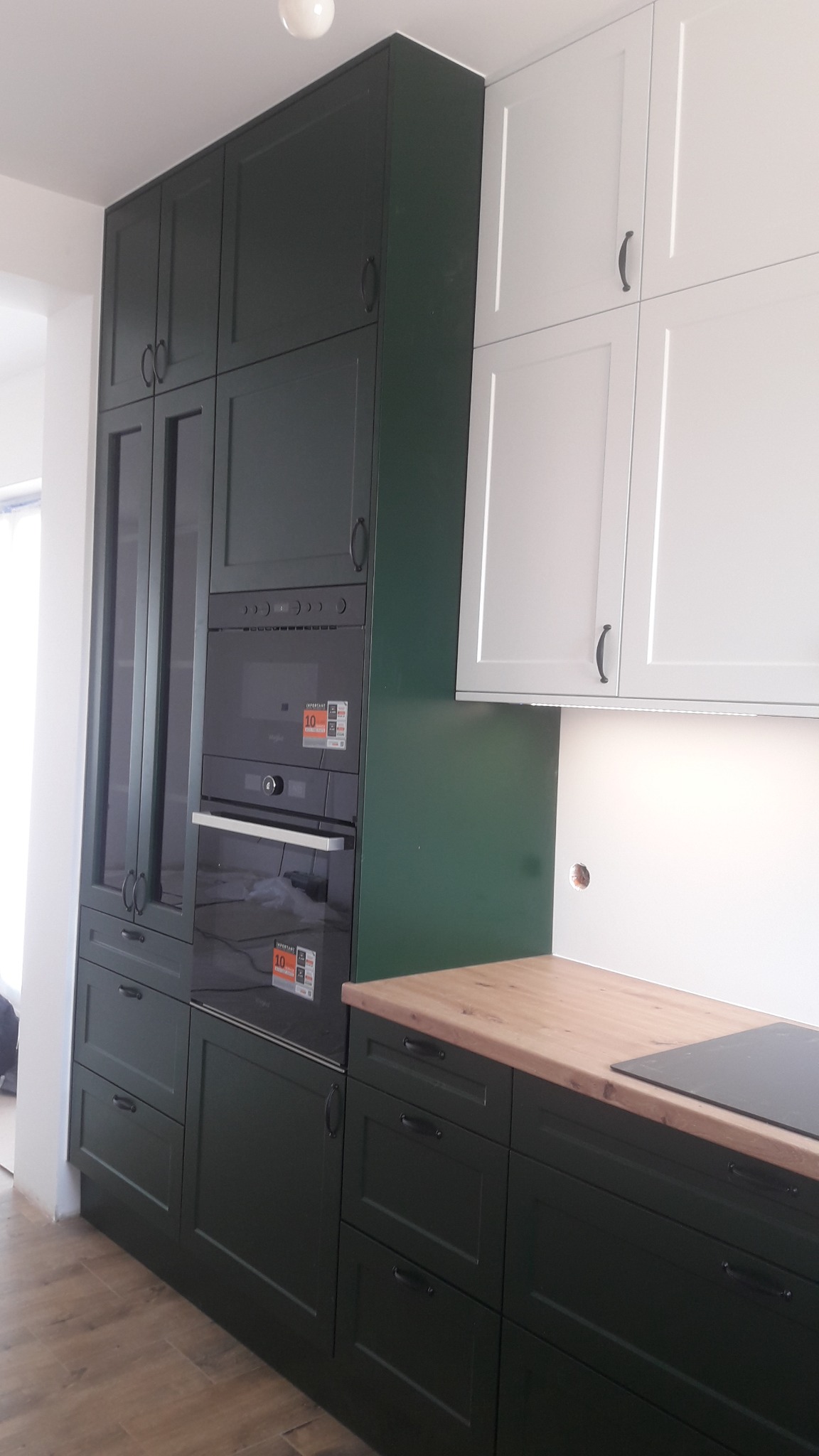 Nowoczesna kuchnia: ciemnozielone szafki dolne i wysokie z piekarnikiem oraz białe szafki górne, drewniany blat.