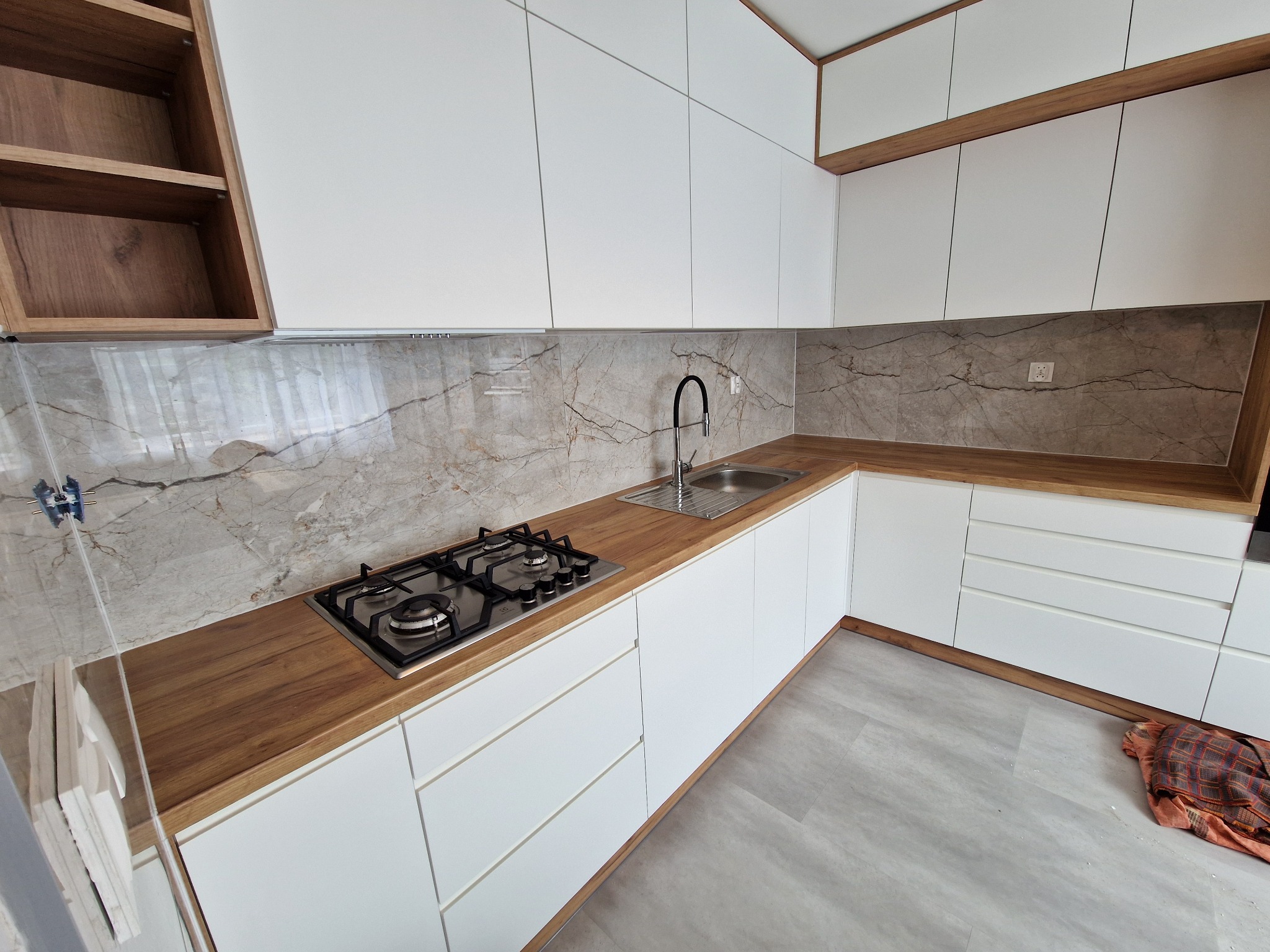 Nowoczesna kuchnia w bieli i drewnie z marmurowym backsplashiem. Uwagę przyciąga minimalistyczny design i oświetlenie LED pod szafkami.