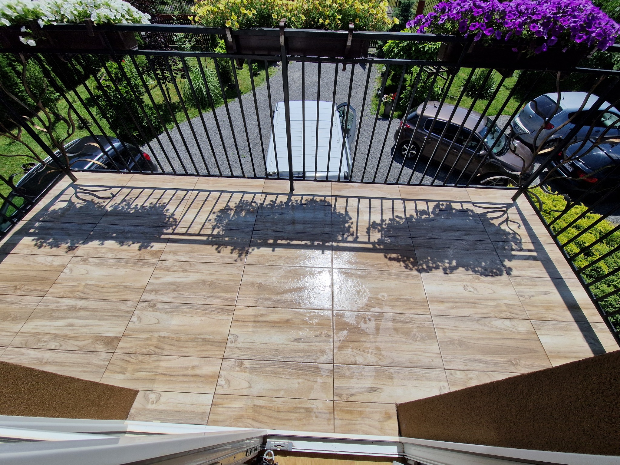 Ułożone płytki imitujące drewno na balkonie w Nowosielcu, widok z góry na balustradę i otoczenie domu. Na balustradzie donice z kwiatami.