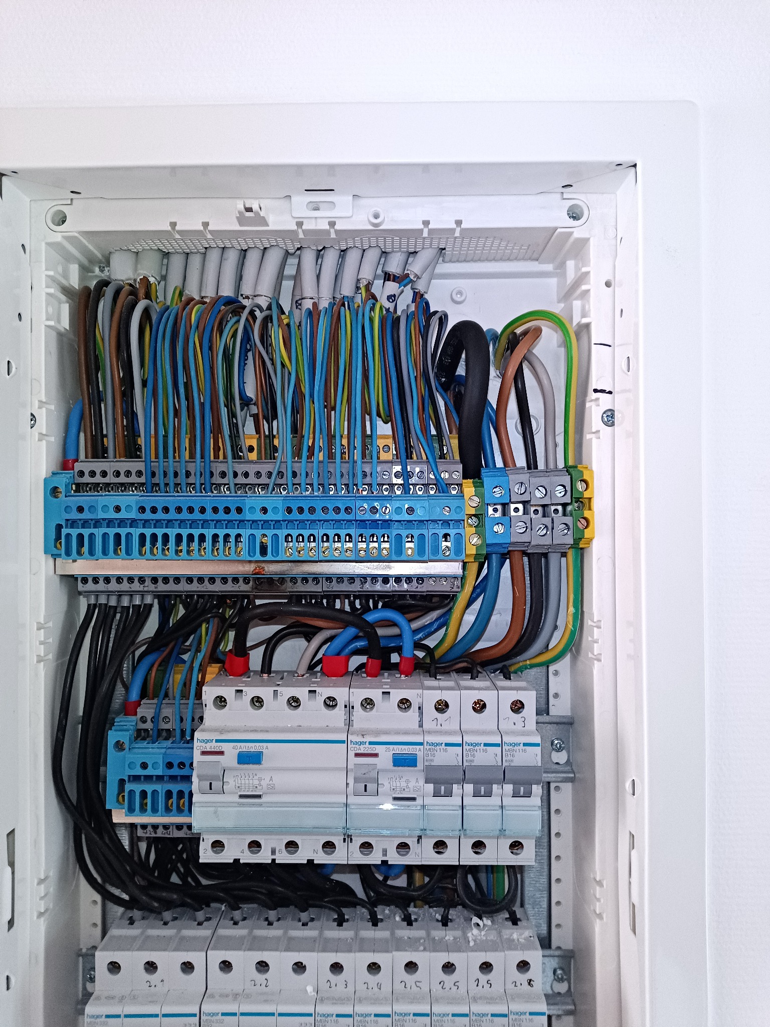 Rozdzielnia elektryczna Hager z widocznymi zabezpieczeniami, listwami zaciskowymi i uporządkowanym okablowaniem w kolorach: niebieskim, brązowym, żółto-zielonym i czarnym.