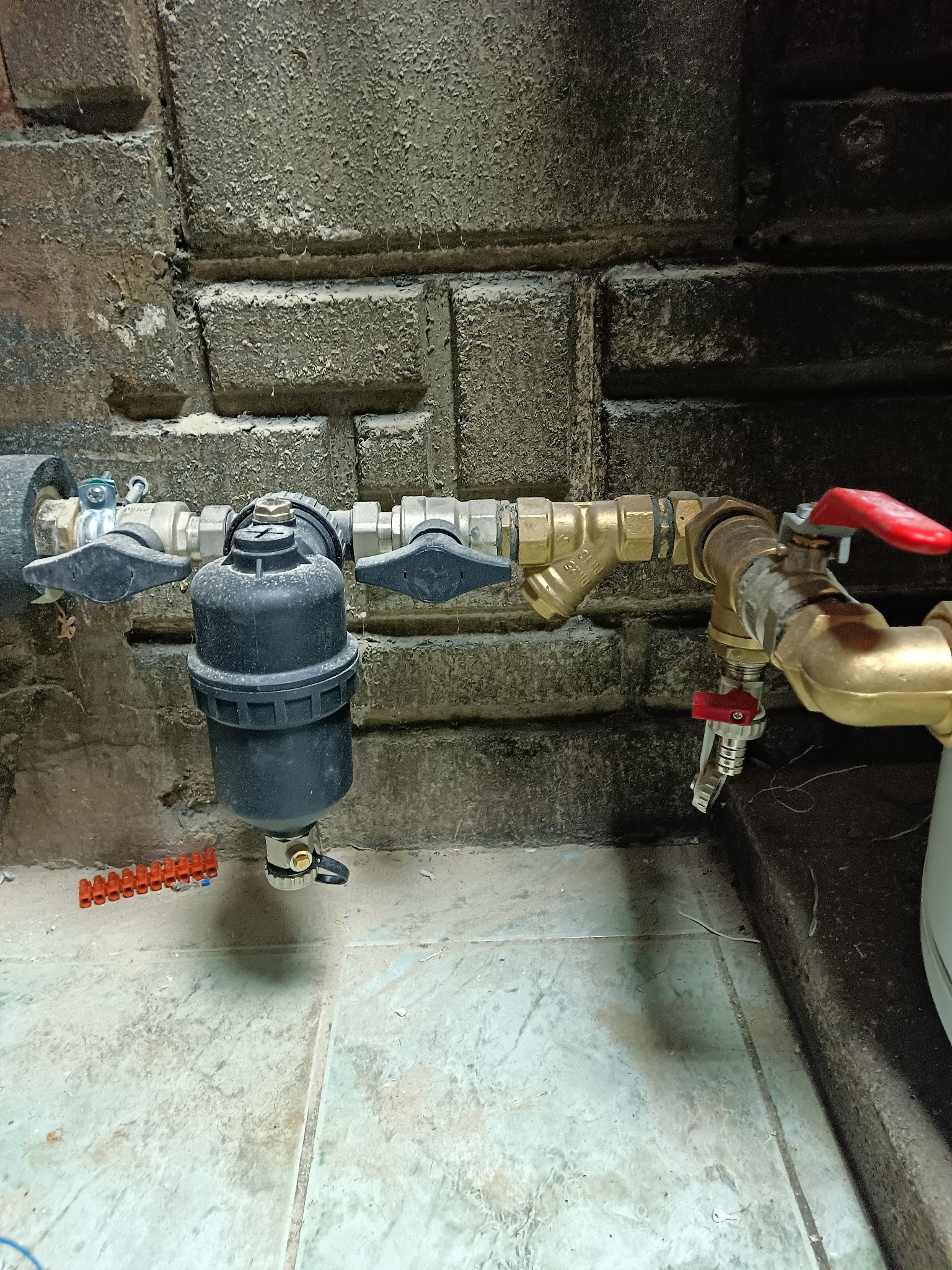 Zamontowany filtr wody z zaworami odcinającymi na tle ściany z cegły. Widoczne złączki i fragment instalacji.
