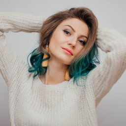 PSPHOTO Studio fotograficzne i filmowe NYSA - Portret młodej kobiety z turkusowymi końcówkami włosów, w kremowym swetrze, pozującej z rękami uniesionymi za głową, na jasnym tle.