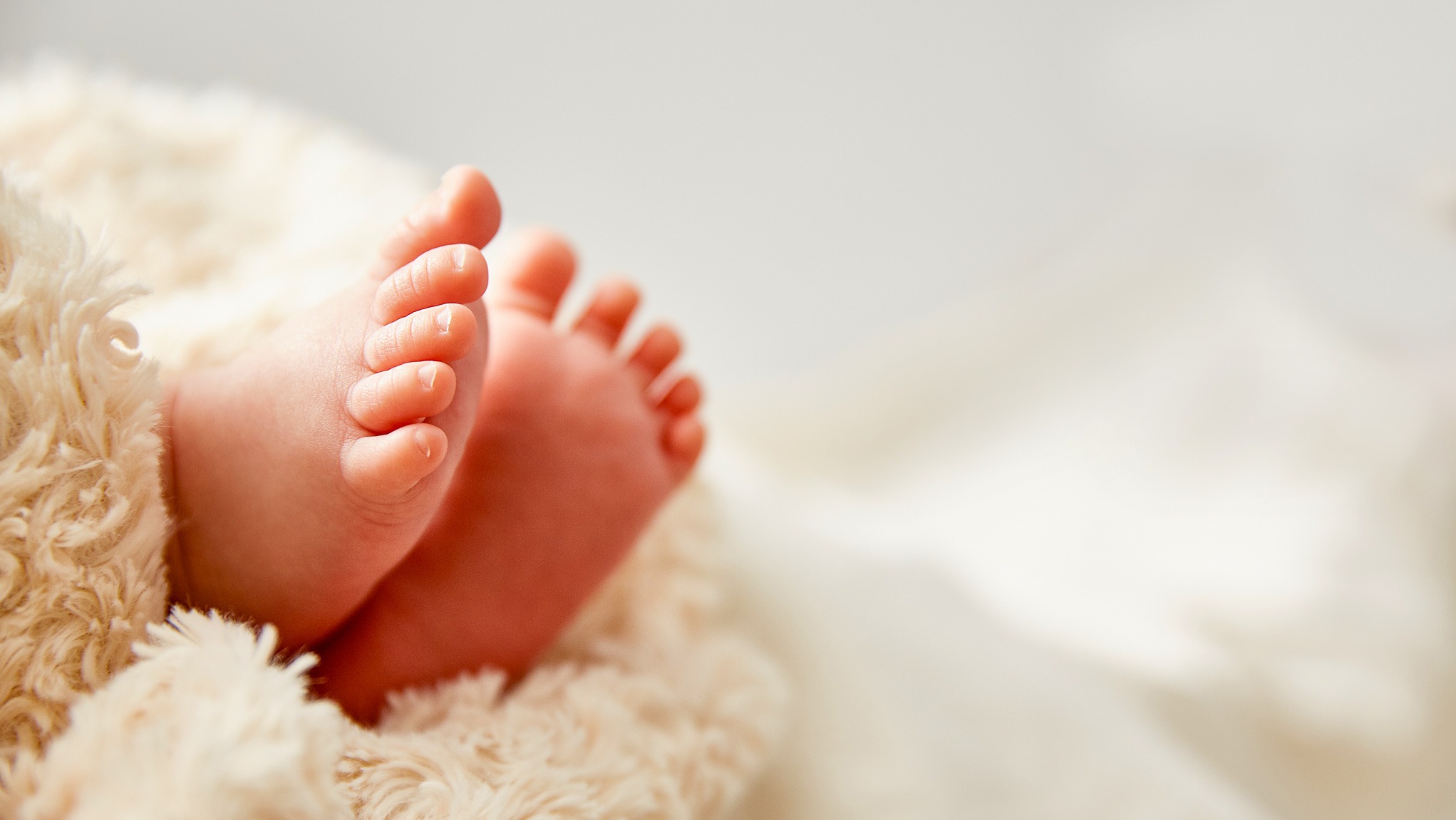 Małe stópki noworodka na miękkim, kremowym kocyku, delikatne światło podkreśla naturalny odcień skóry.