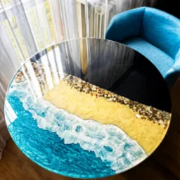 Okrągły blat stolika kawowego z żywicy epoksydowej, imitujący plażę i morze, z widocznymi kamieniami i falami. Wykonanie firmy z Żukowa.